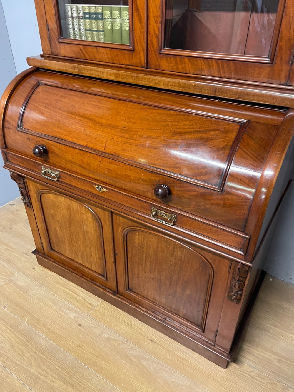 A 19th-century mahogany cylinder bureau bookcase featuring an upper glazed cabinet with two arched doors, a roll-top writing section, and a lower two-door cupboard. View V