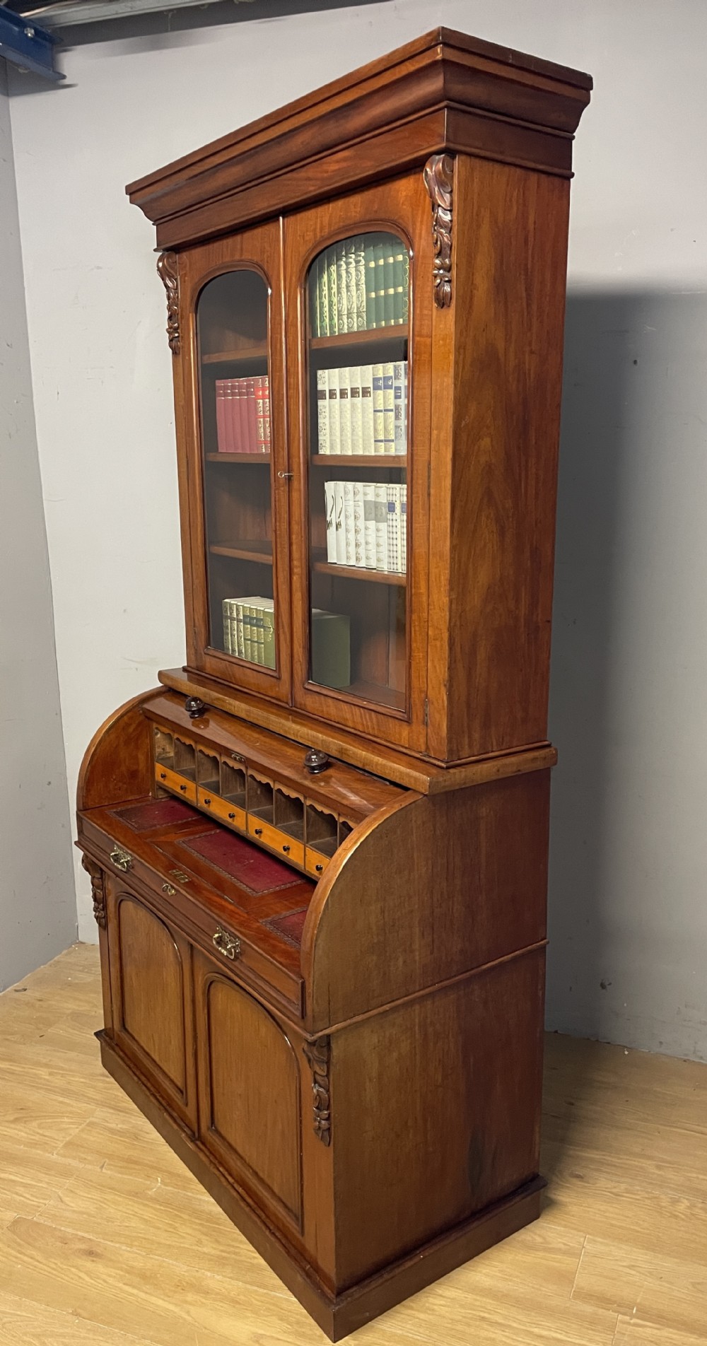 A 19th-century mahogany cylinder bureau bookcase featuring an upper glazed cabinet with two arched doors, a roll-top writing section, and a lower two-door cupboard. View XII