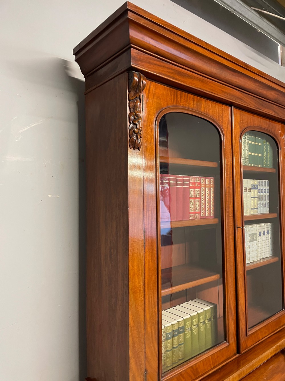 A 19th-century mahogany cylinder bureau bookcase featuring an upper glazed cabinet with two arched doors, a roll-top writing section, and a lower two-door cupboard. View XV