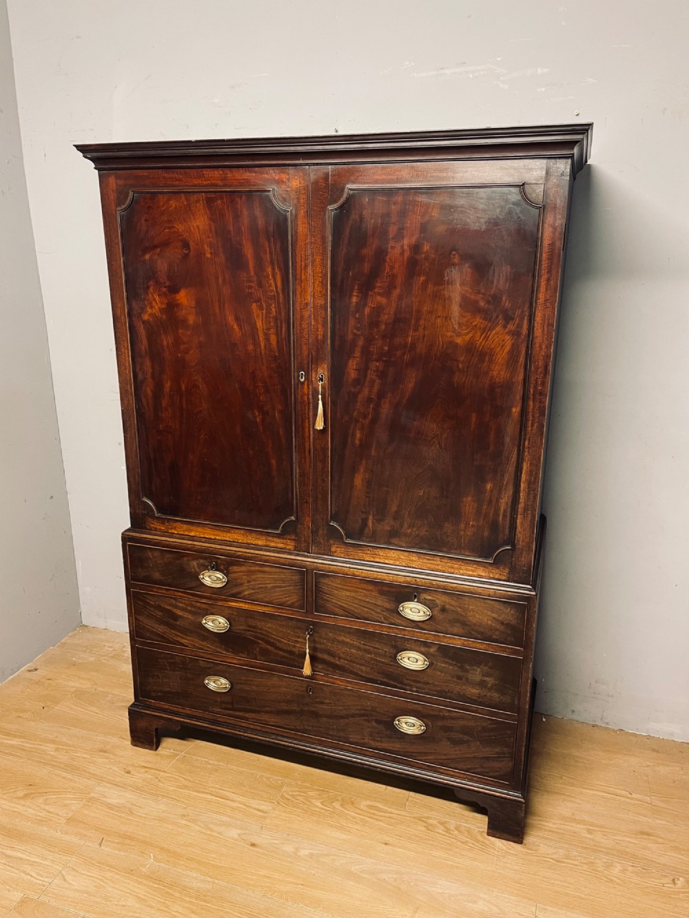 A Georgian flame mahogany linen press featuring an upper double-door cupboard with panelled doors above a lower chest of drawers with oval brass handles.