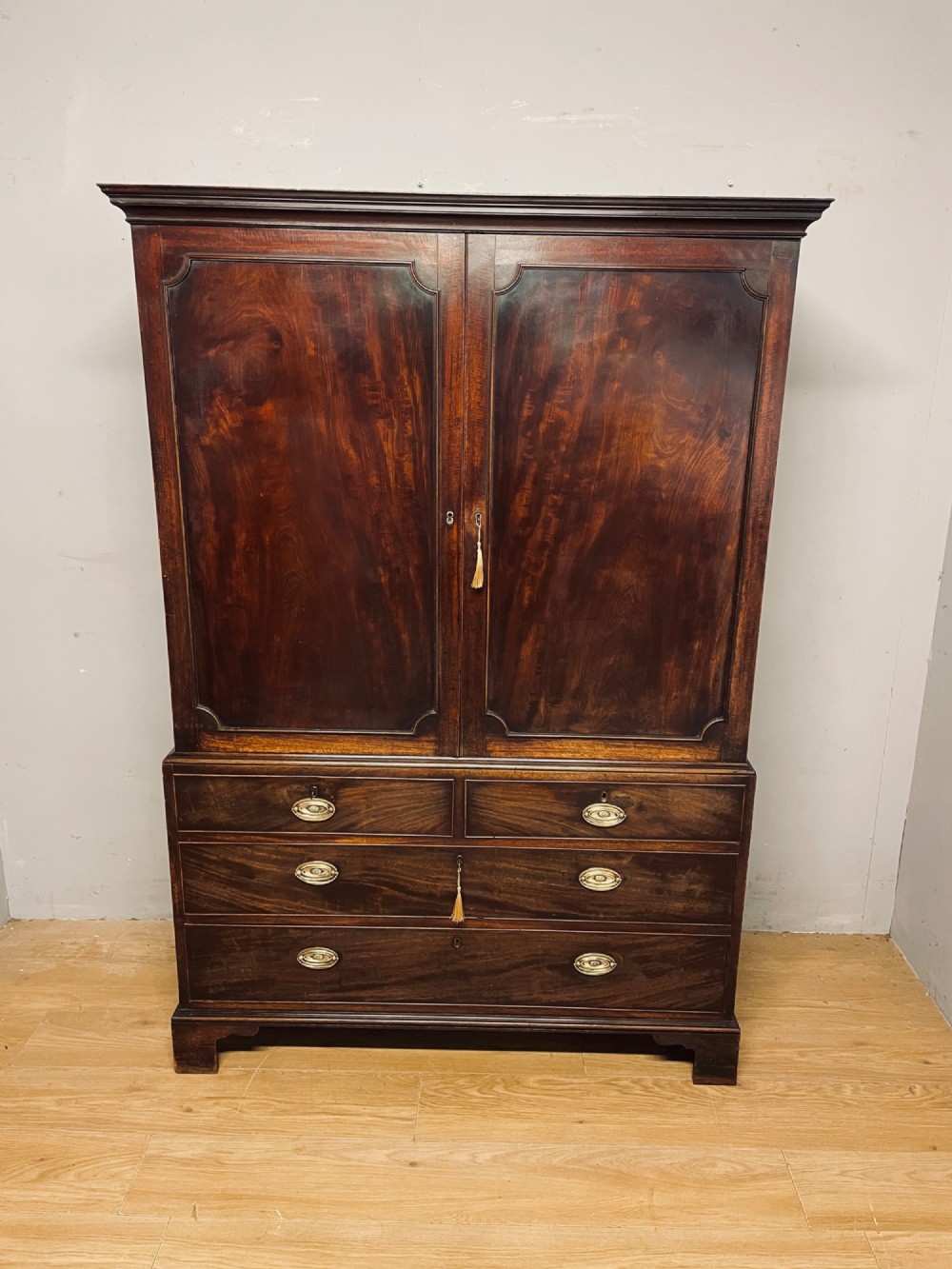 A Georgian flame mahogany linen press featuring an upper double-door cupboard with panelled doors above a lower chest of drawers with oval brass handles. View II