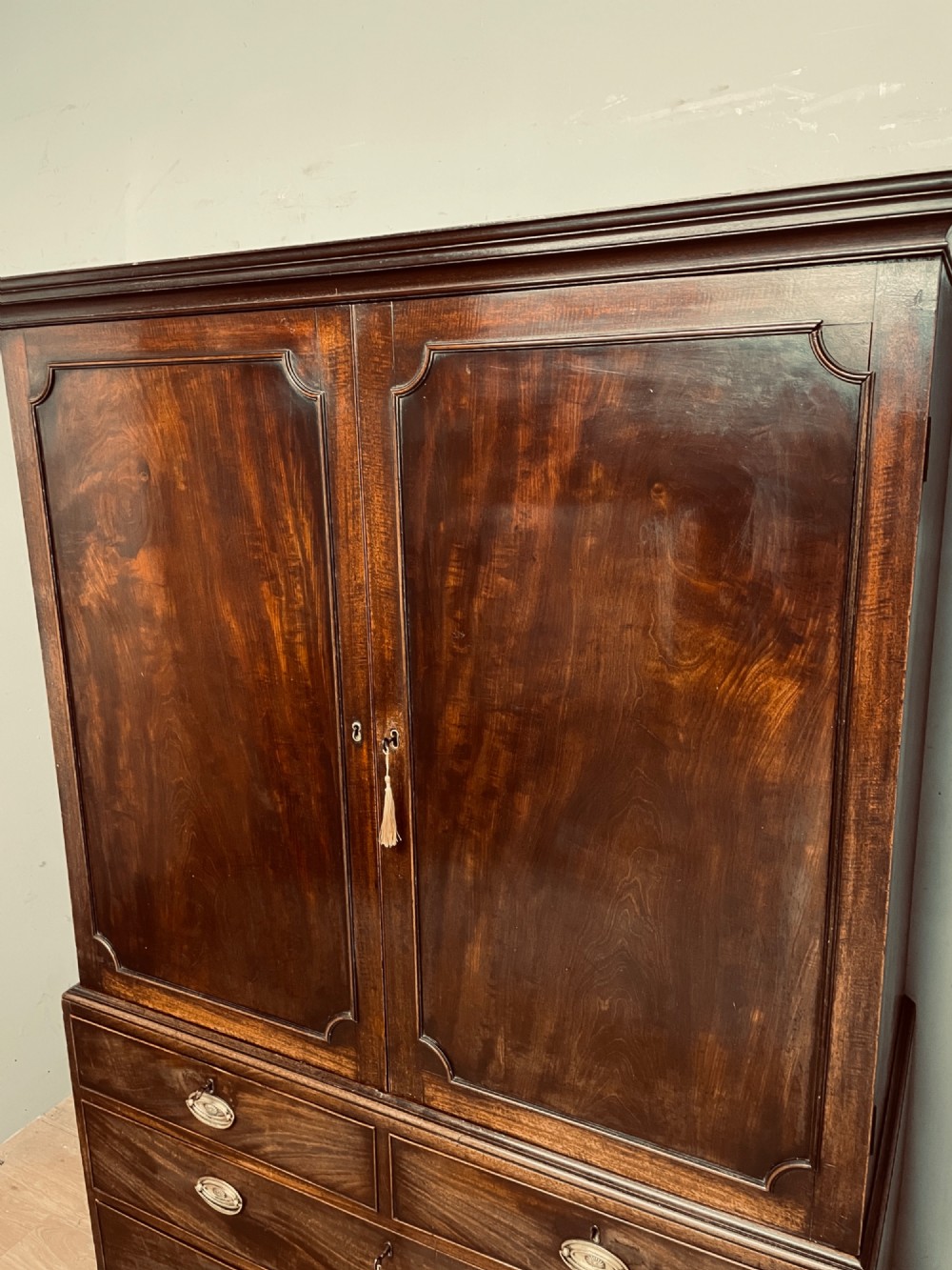A Georgian flame mahogany linen press featuring an upper double-door cupboard with panelled doors above a lower chest of drawers with oval brass handles. View III