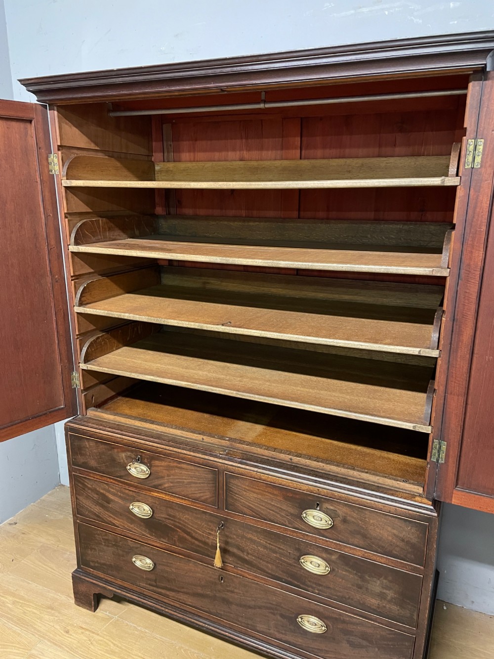 A Georgian flame mahogany linen press featuring an upper double-door cupboard with panelled doors above a lower chest of drawers with oval brass handles. View IV
