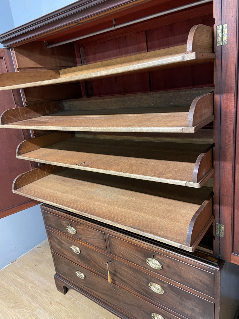 A Georgian flame mahogany linen press featuring an upper double-door cupboard with panelled doors above a lower chest of drawers with oval brass handles. View V