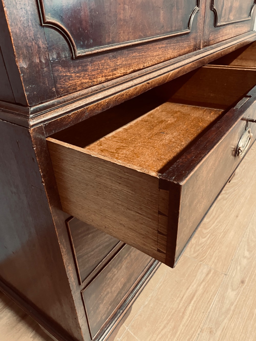 A Georgian flame mahogany linen press featuring an upper double-door cupboard with panelled doors above a lower chest of drawers with oval brass handles. View VI