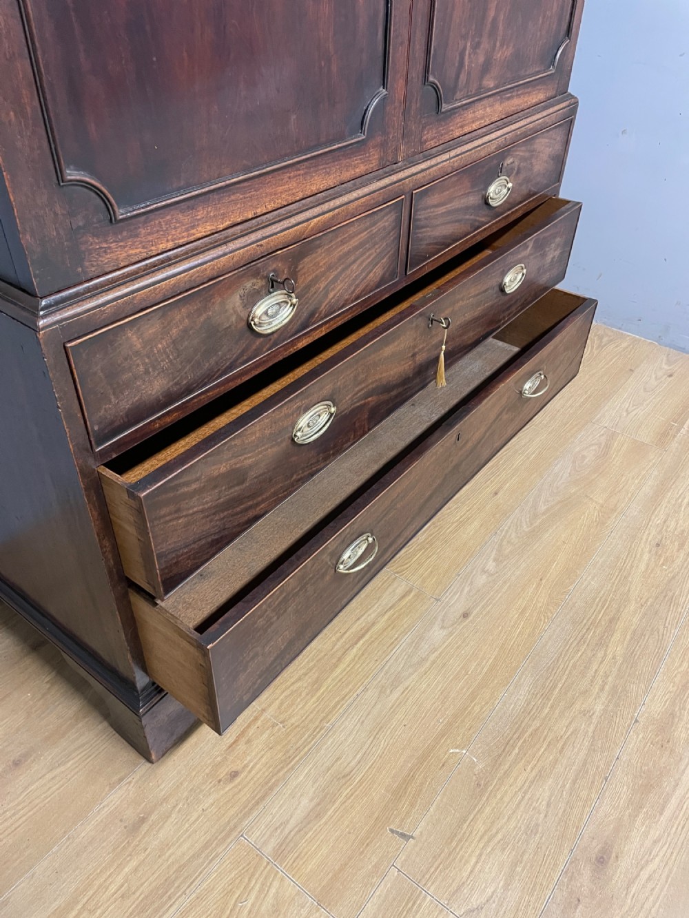 A Georgian flame mahogany linen press featuring an upper double-door cupboard with panelled doors above a lower chest of drawers with oval brass handles. View VII