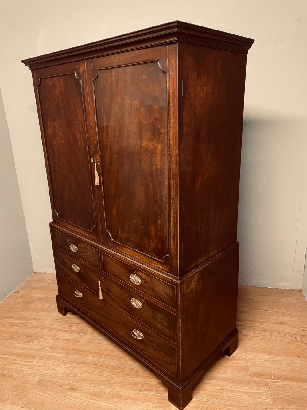 A Georgian flame mahogany linen press featuring an upper double-door cupboard with panelled doors above a lower chest of drawers with oval brass handles. View VIII