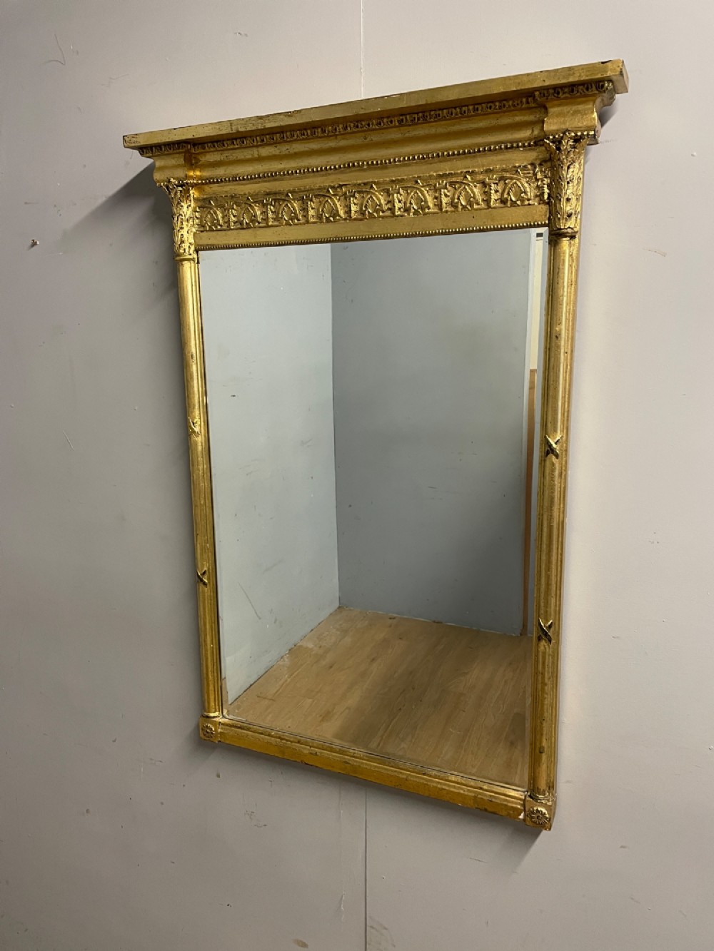 A rectangular giltwood wall mirror featuring a projecting cornice top, classical column pilasters, arcaded frieze details, and rosette corner blocks.
