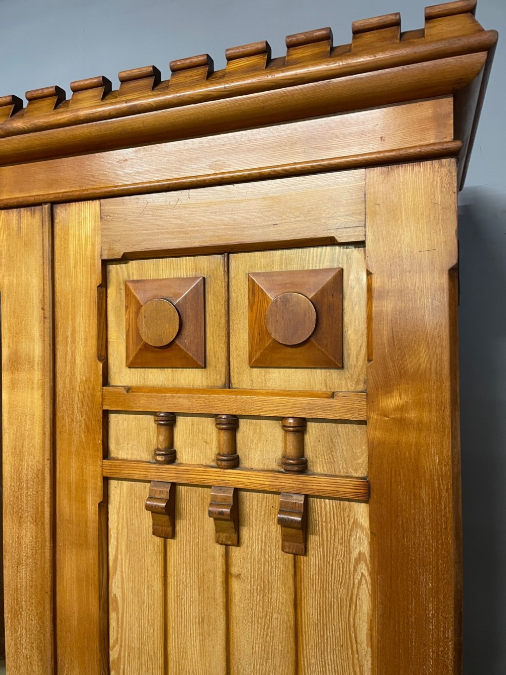 A large golden ash Arts and Crafts triple wardrobe featuring a central mirrored door flanked by panelled wooden doors with castellated cornice detailing. View III