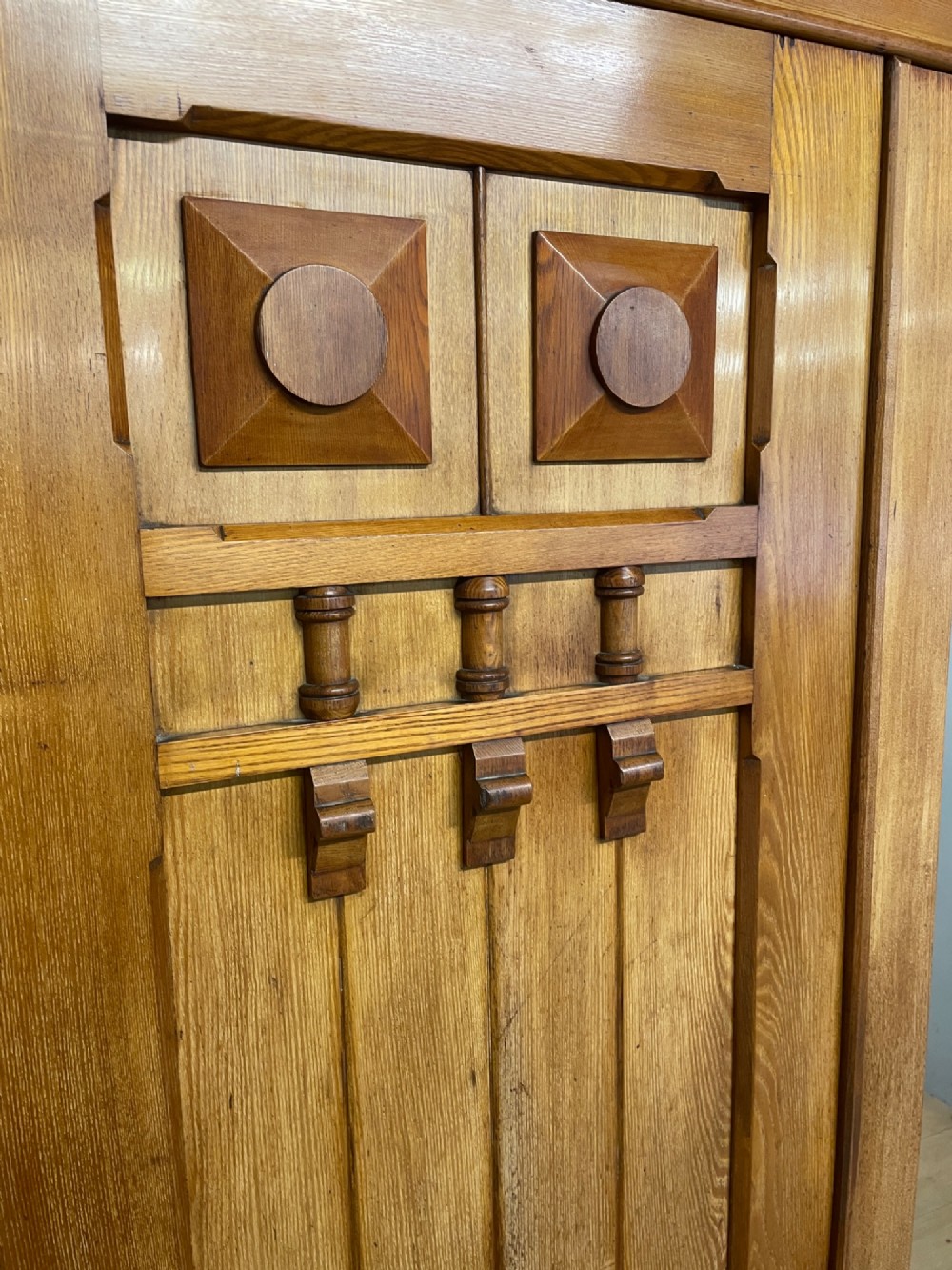 A large golden ash Arts and Crafts triple wardrobe featuring a central mirrored door flanked by panelled wooden doors with castellated cornice detailing. View VI
