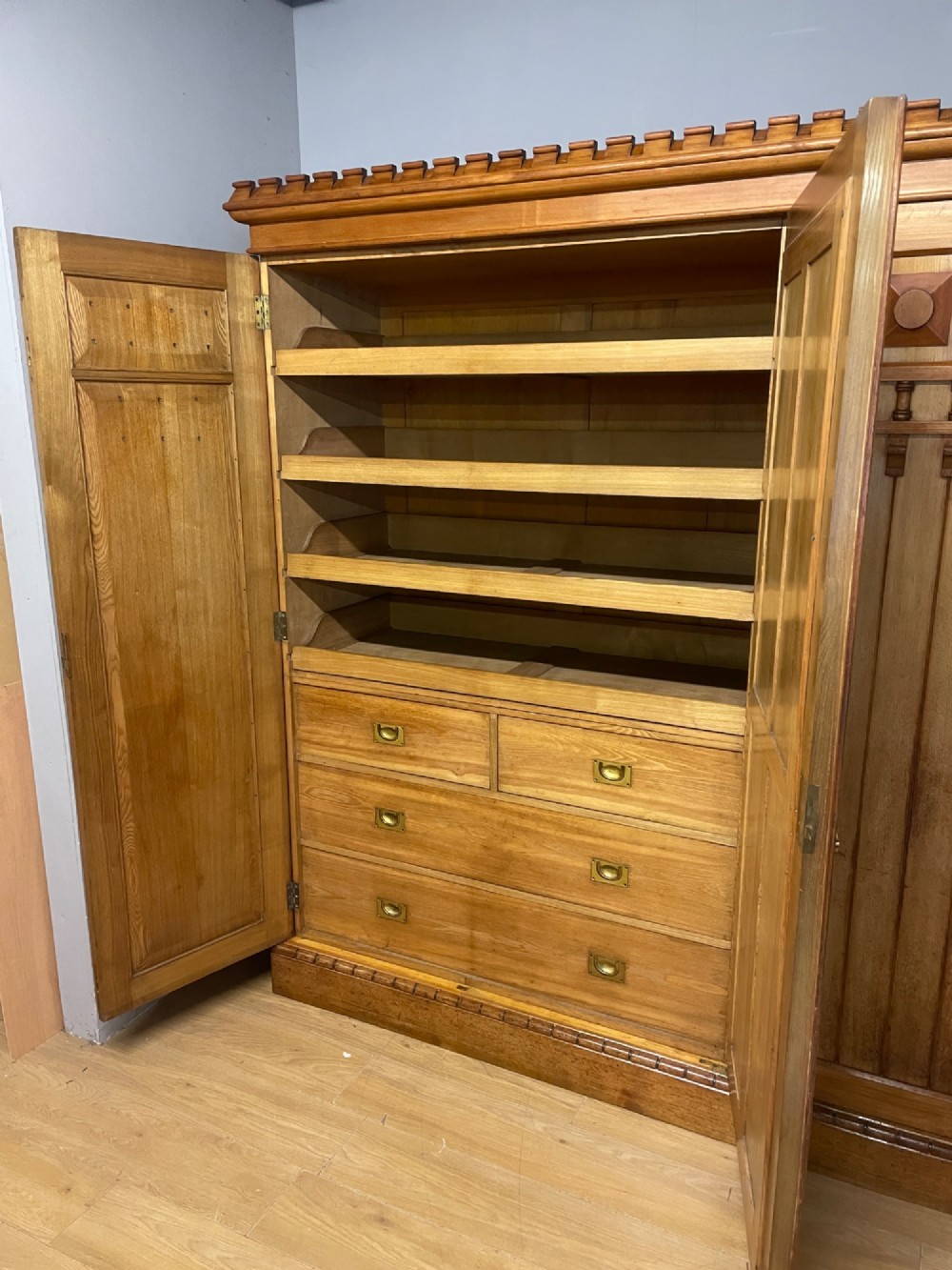 A large golden ash Arts and Crafts triple wardrobe featuring a central mirrored door flanked by panelled wooden doors with castellated cornice detailing. View VII