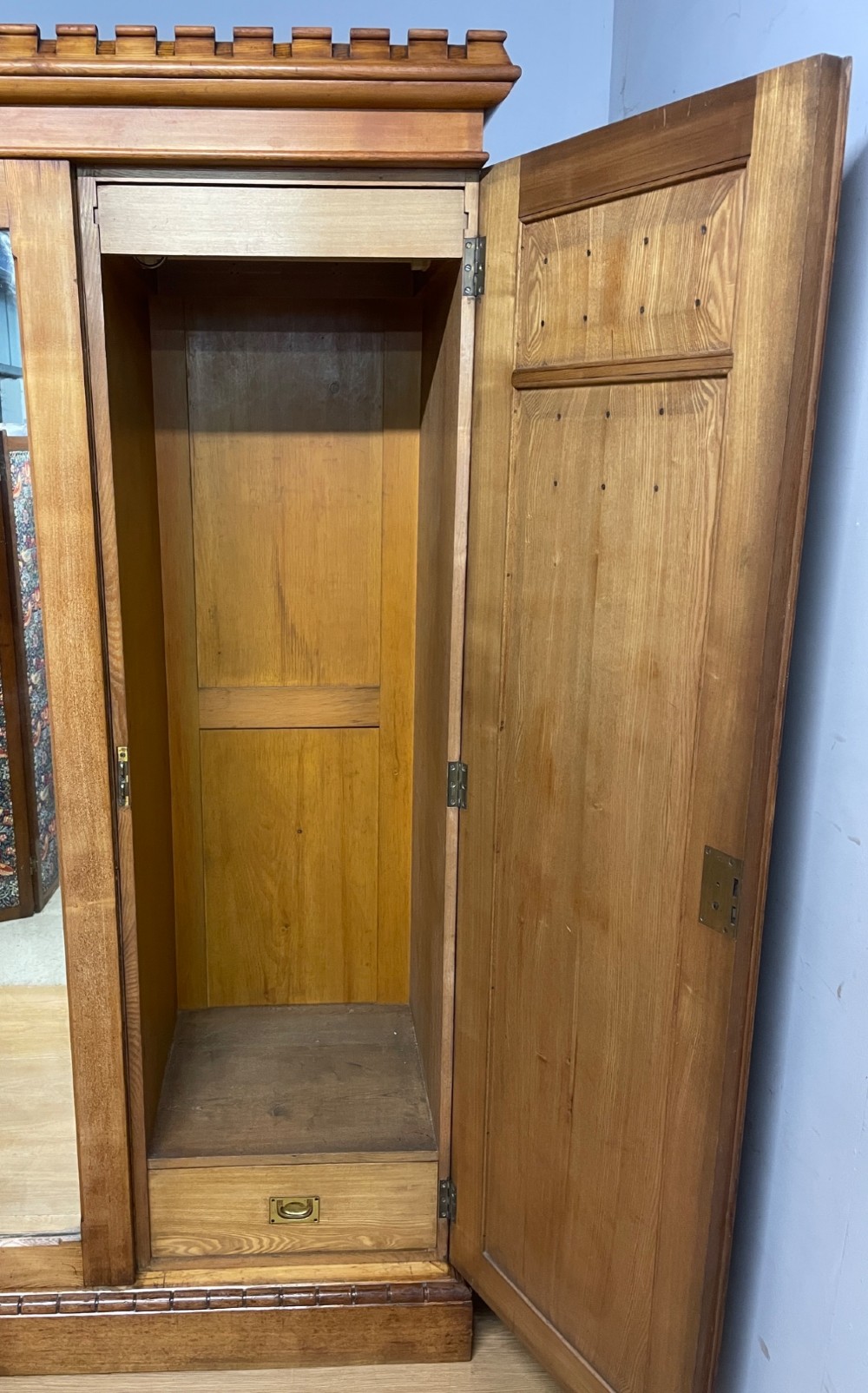 A large golden ash Arts and Crafts triple wardrobe featuring a central mirrored door flanked by panelled wooden doors with castellated cornice detailing. View VIII