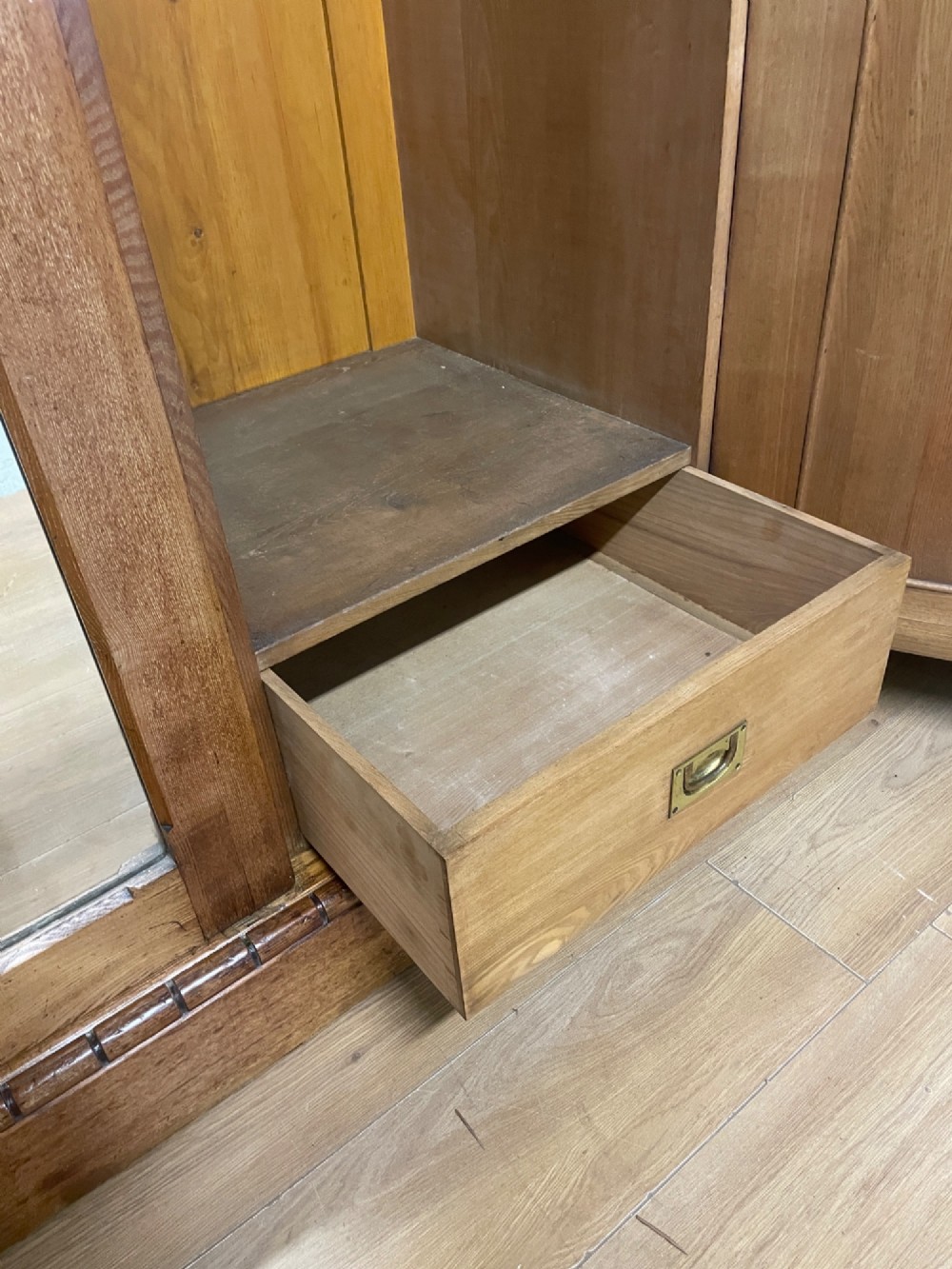 A large golden ash Arts and Crafts triple wardrobe featuring a central mirrored door flanked by panelled wooden doors with castellated cornice detailing. View X