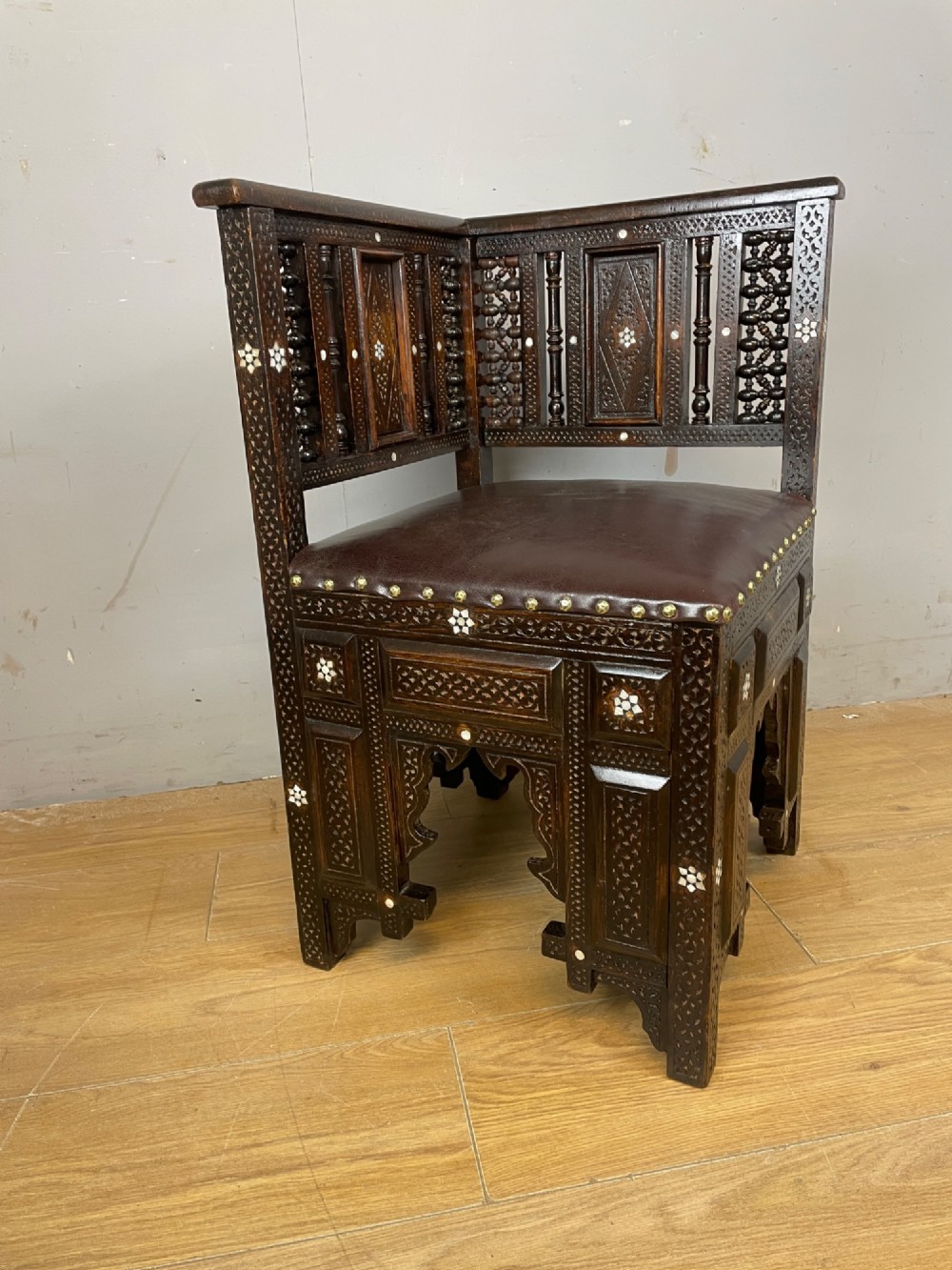 A 19th-century carved dark wood corner chair featuring mother-of-pearl floral inlay, detailed Mashrabiya panels, and a brown leather seat secured with brass studs. View III