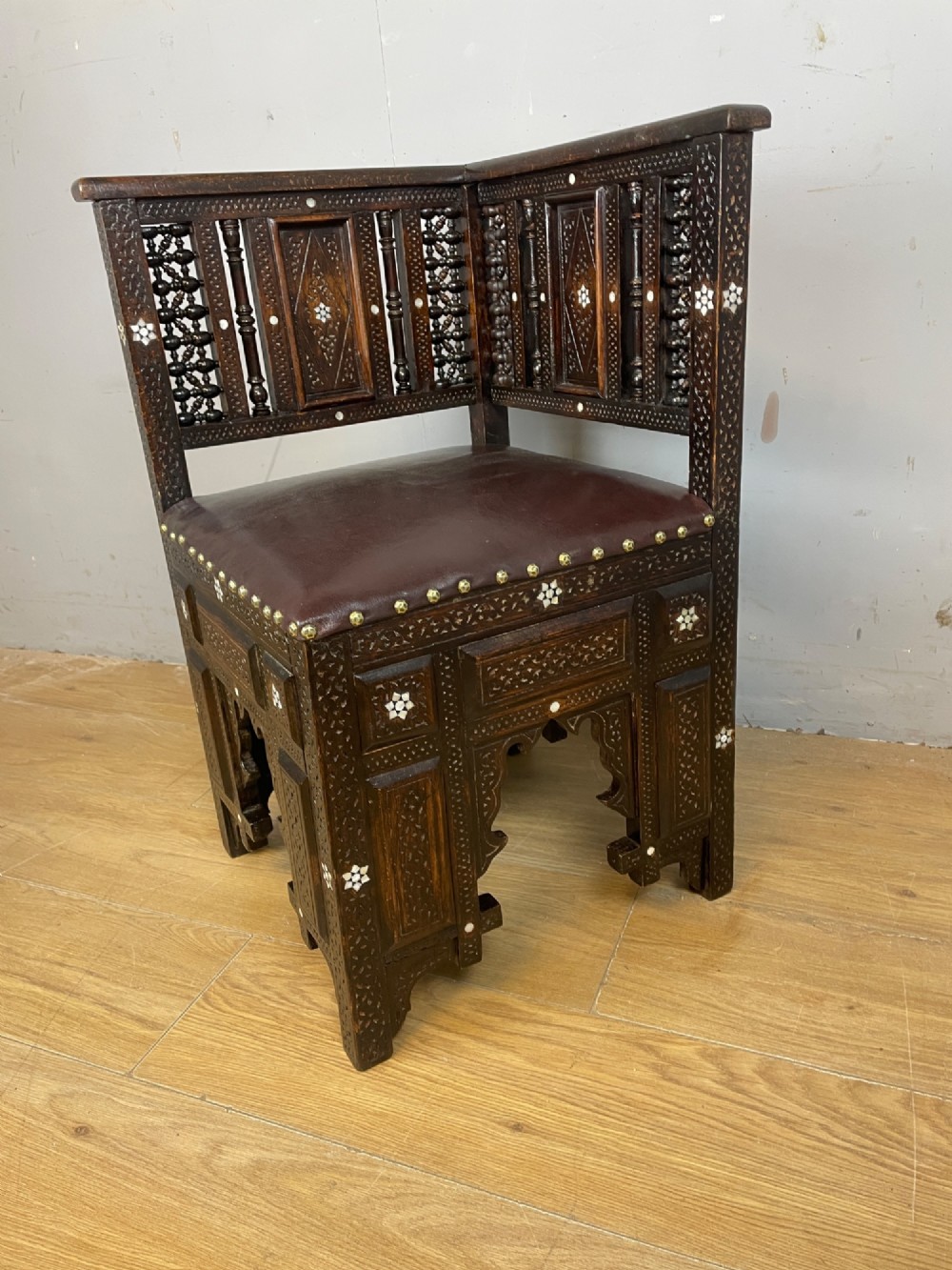 A 19th-century carved dark wood corner chair featuring mother-of-pearl floral inlay, detailed Mashrabiya panels, and a brown leather seat secured with brass studs. View IV