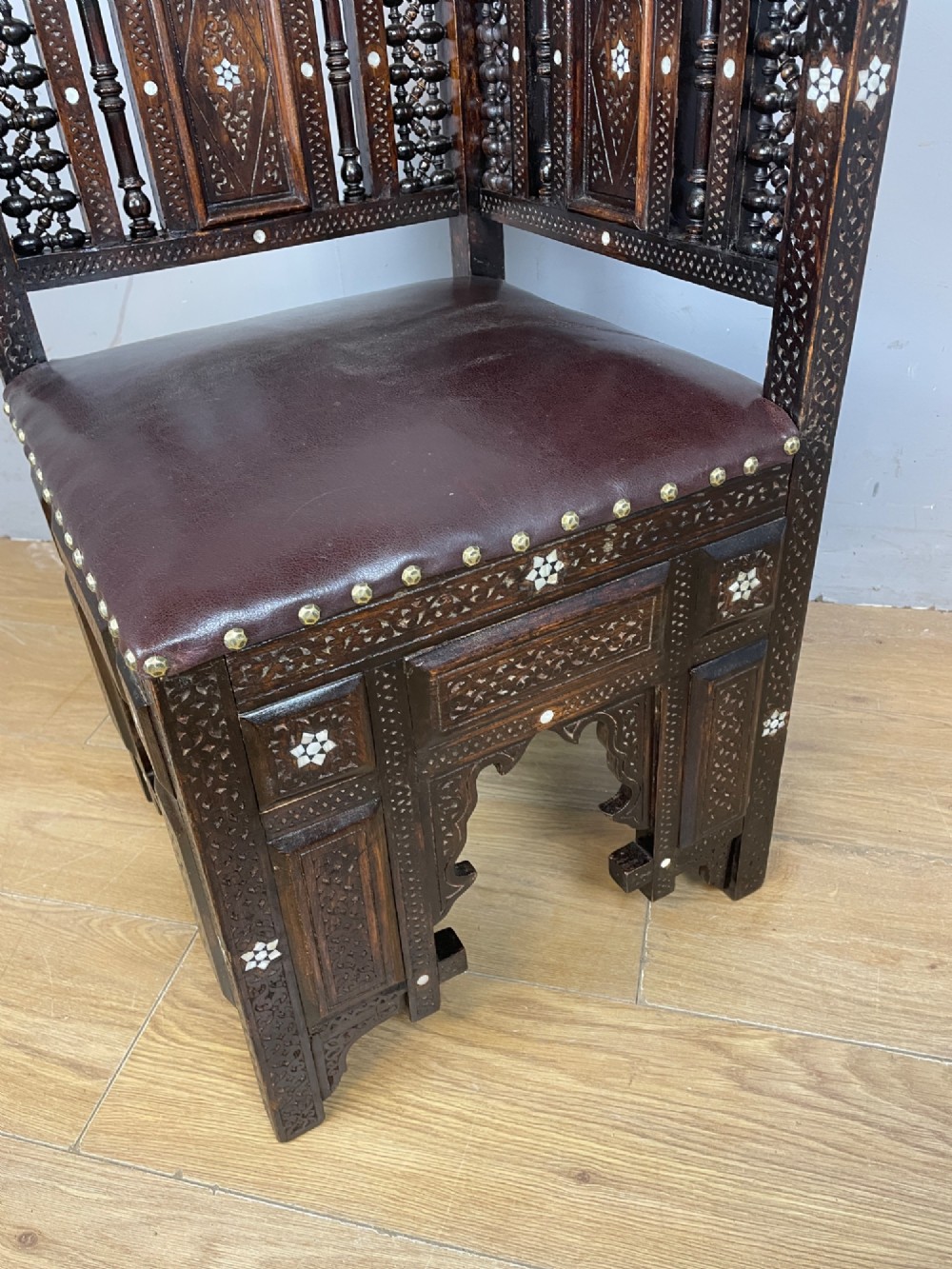 A 19th-century carved dark wood corner chair featuring mother-of-pearl floral inlay, detailed Mashrabiya panels, and a brown leather seat secured with brass studs. View VIII