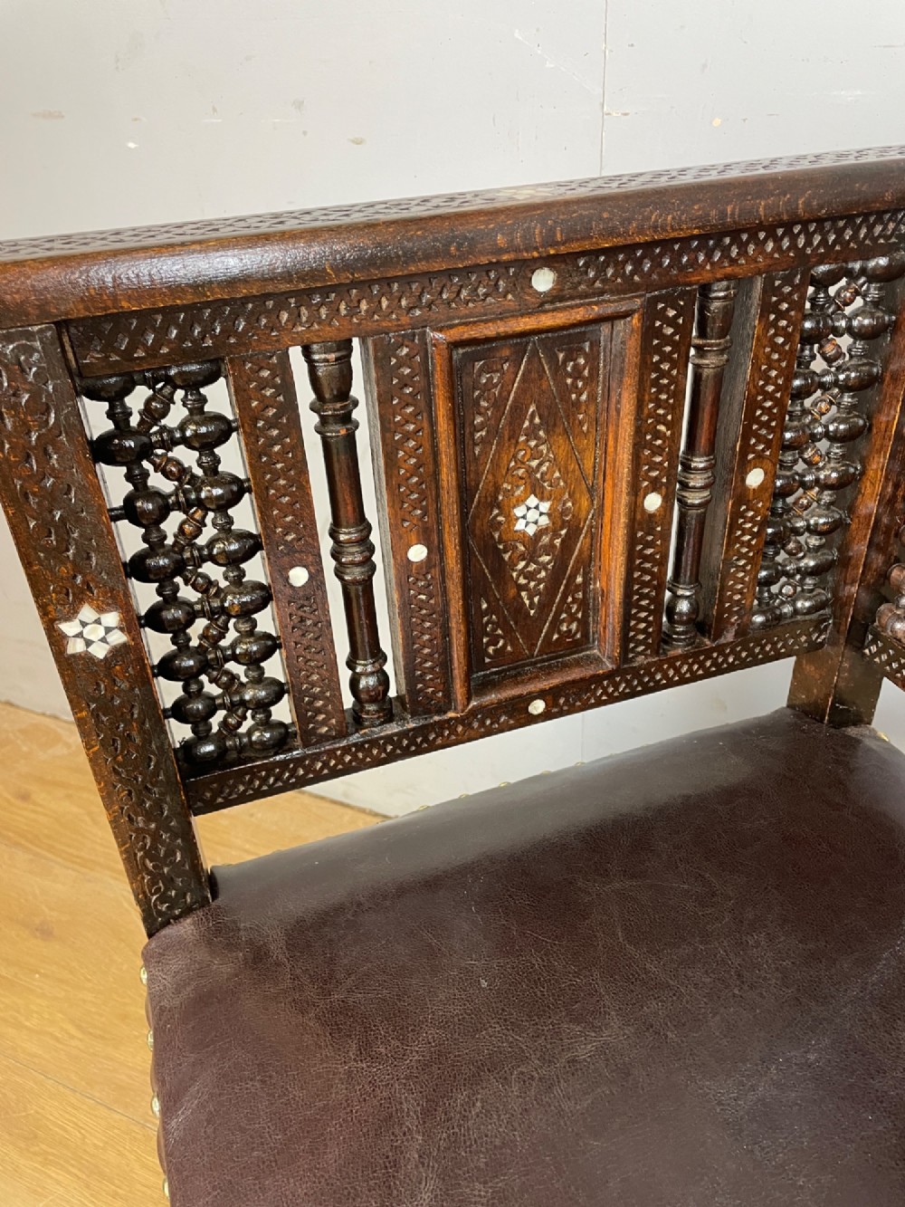 A 19th-century carved dark wood corner chair featuring mother-of-pearl floral inlay, detailed Mashrabiya panels, and a brown leather seat secured with brass studs. View IX
