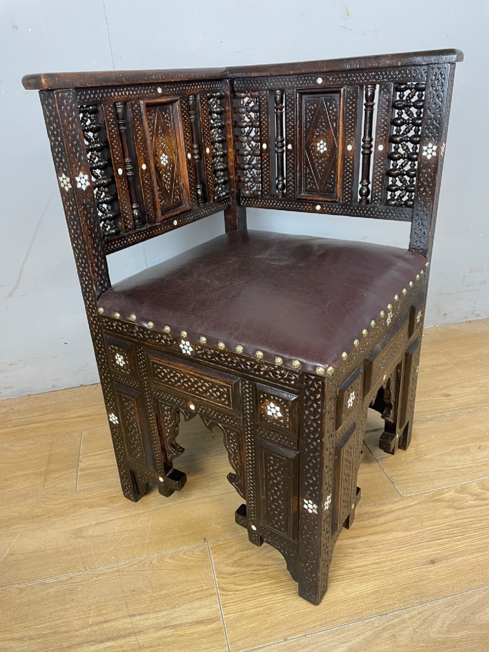 A 19th-century carved dark wood corner chair featuring mother-of-pearl floral inlay, detailed Mashrabiya panels, and a brown leather seat secured with brass studs. View XI