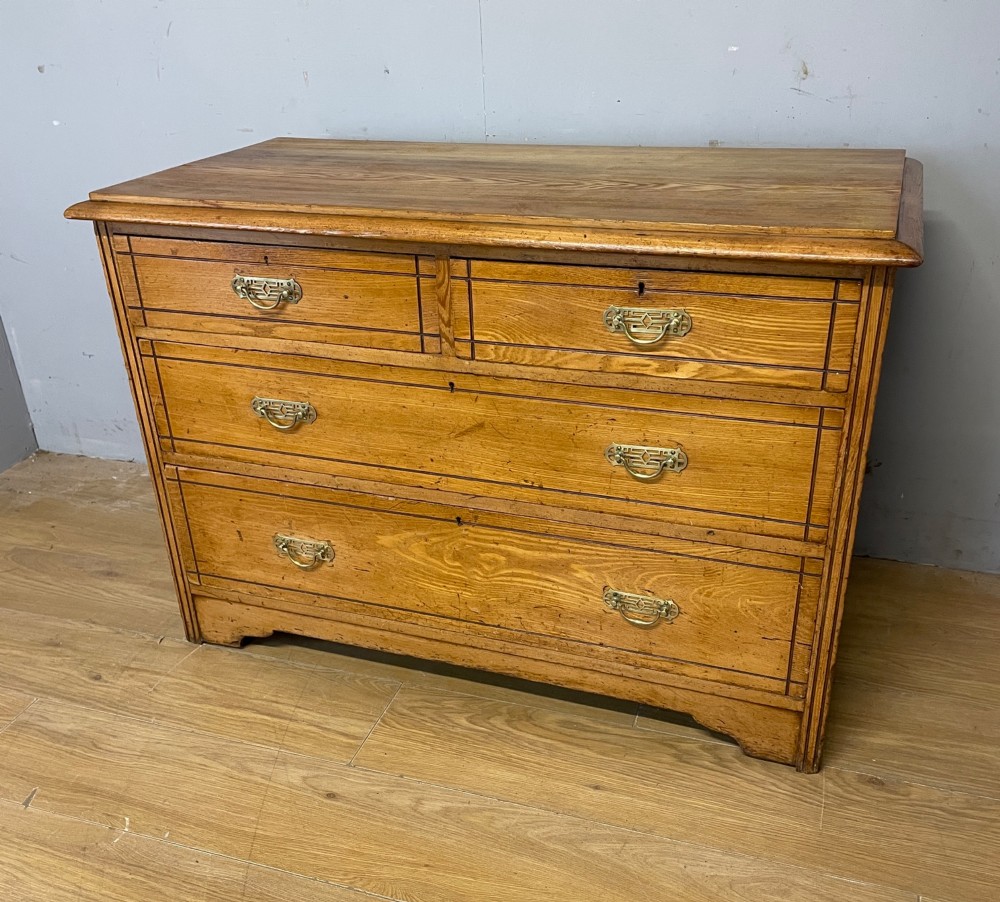 An Arts and Crafts solid ash chest of drawers featuring two short drawers over two long drawers with brass drop handles and dark linear inlay.