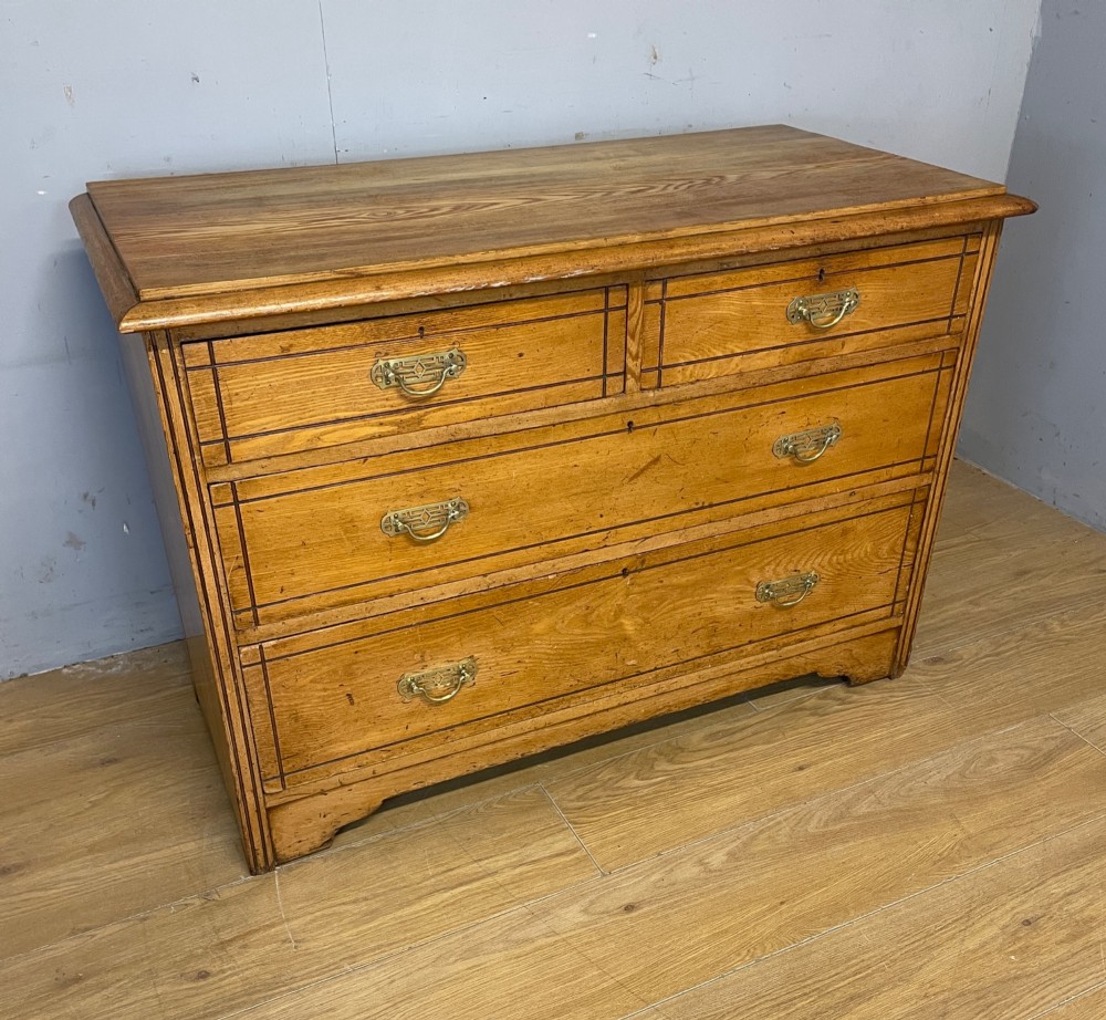 An Arts and Crafts solid ash chest of drawers featuring two short drawers over two long drawers with brass drop handles and dark linear inlay. View II