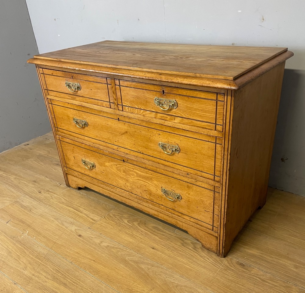 An Arts and Crafts solid ash chest of drawers featuring two short drawers over two long drawers with brass drop handles and dark linear inlay. View IV