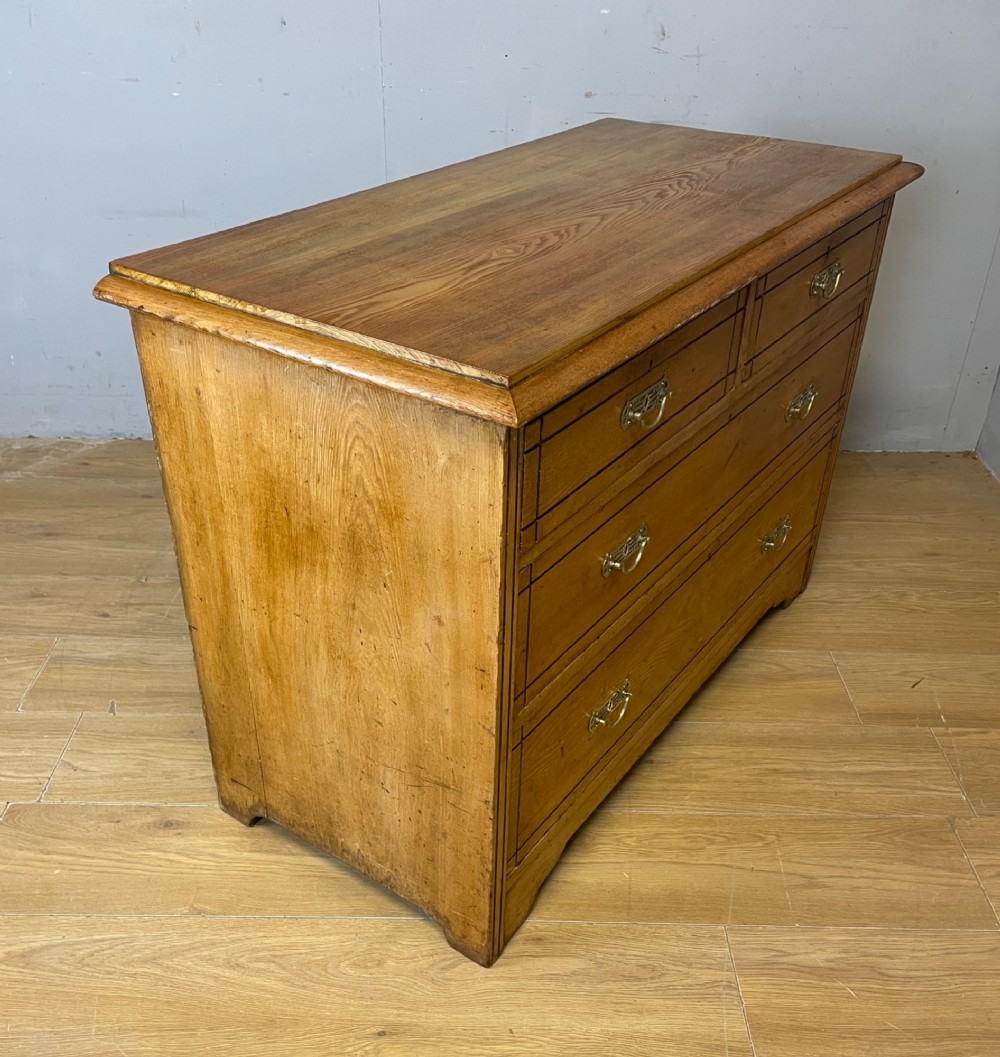 An Arts and Crafts solid ash chest of drawers featuring two short drawers over two long drawers with brass drop handles and dark linear inlay. View VI
