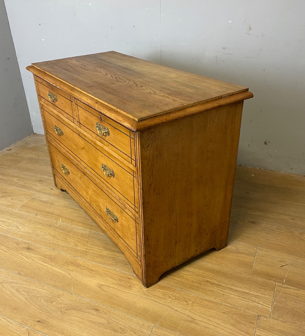 An Arts and Crafts solid ash chest of drawers featuring two short drawers over two long drawers with brass drop handles and dark linear inlay. View VII