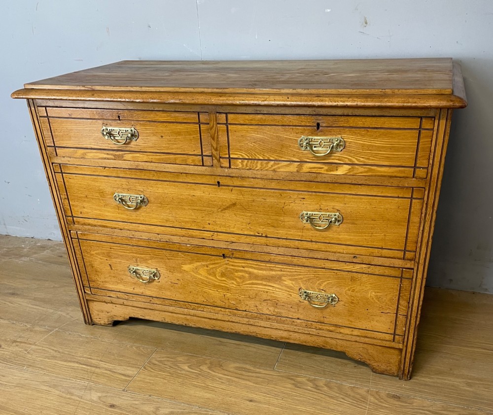 An Arts and Crafts solid ash chest of drawers featuring two short drawers over two long drawers with brass drop handles and dark linear inlay. View IX