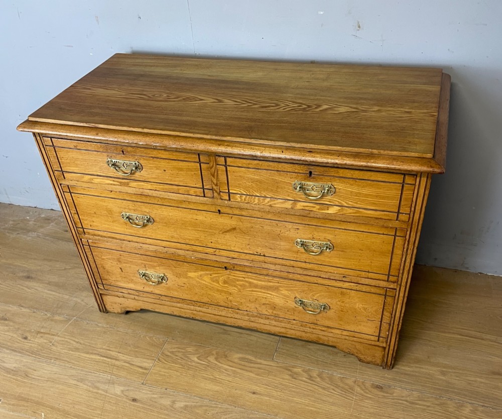 An Arts and Crafts solid ash chest of drawers featuring two short drawers over two long drawers with brass drop handles and dark linear inlay. View X