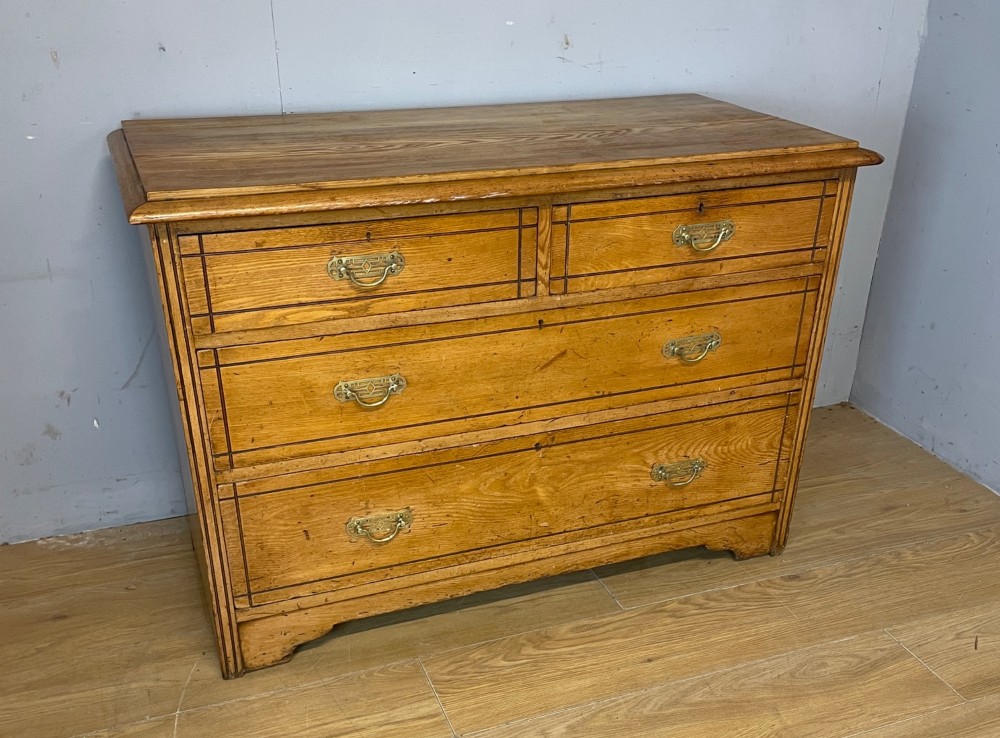 An Arts and Crafts solid ash chest of drawers featuring two short drawers over two long drawers with brass drop handles and dark linear inlay. View XI