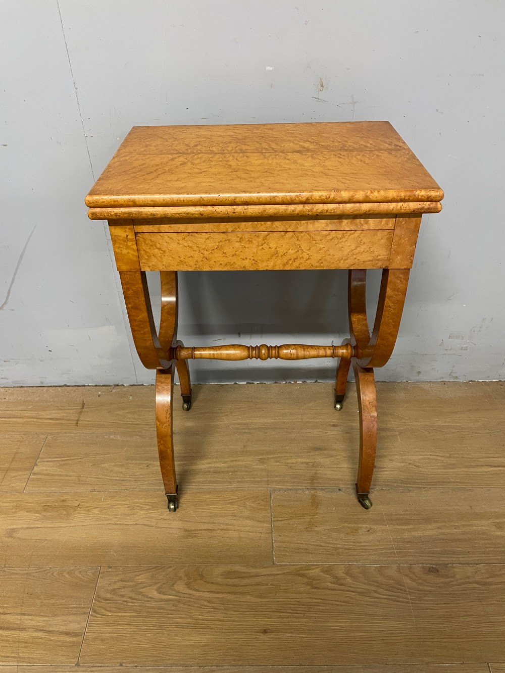 A 19th-century Biedermeier birds eye maple card table featuring a rectangular fold-over top, sweeping legs, a turned central stretcher, and brass castors. View II