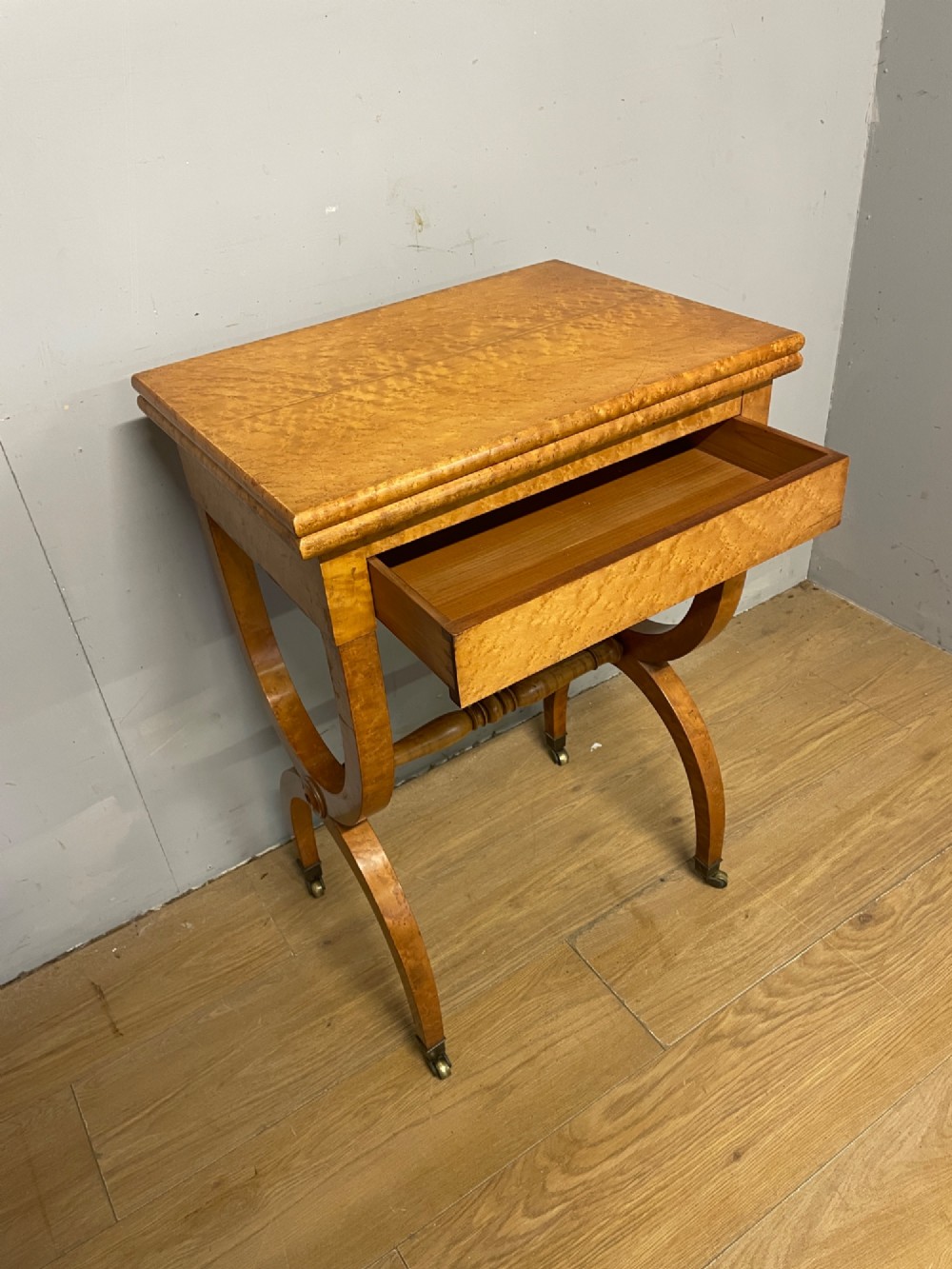 A 19th-century Biedermeier birds eye maple card table featuring a rectangular fold-over top, sweeping legs, a turned central stretcher, and brass castors. View III