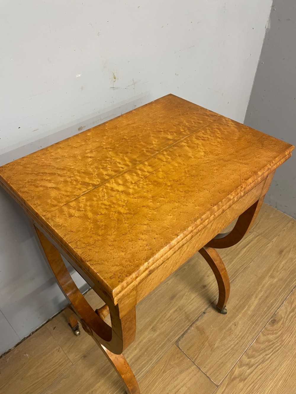 A 19th-century Biedermeier birds eye maple card table featuring a rectangular fold-over top, sweeping legs, a turned central stretcher, and brass castors. View IV