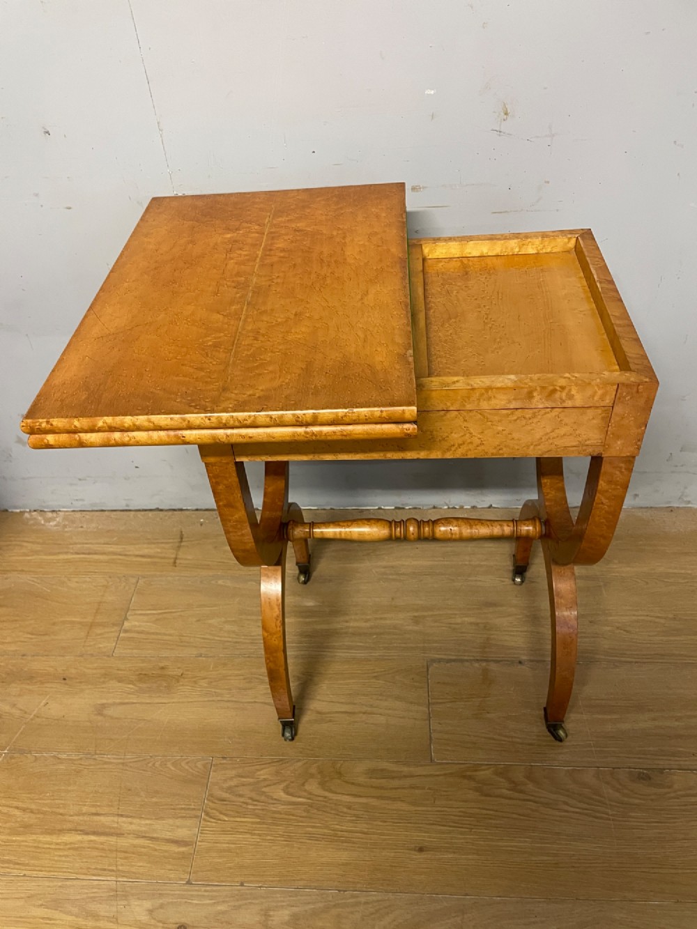 A 19th-century Biedermeier birds eye maple card table featuring a rectangular fold-over top, sweeping legs, a turned central stretcher, and brass castors. View V