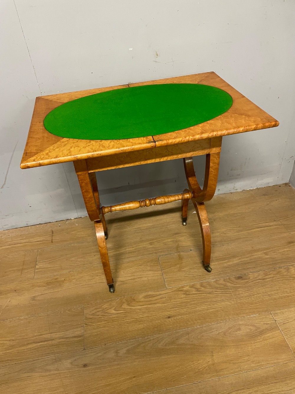 A 19th-century Biedermeier birds eye maple card table featuring a rectangular fold-over top, sweeping legs, a turned central stretcher, and brass castors. View VI