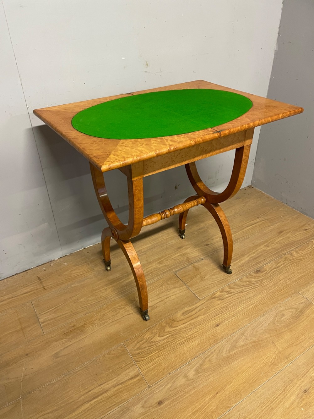 A 19th-century Biedermeier birds eye maple card table featuring a rectangular fold-over top, sweeping legs, a turned central stretcher, and brass castors. View VII