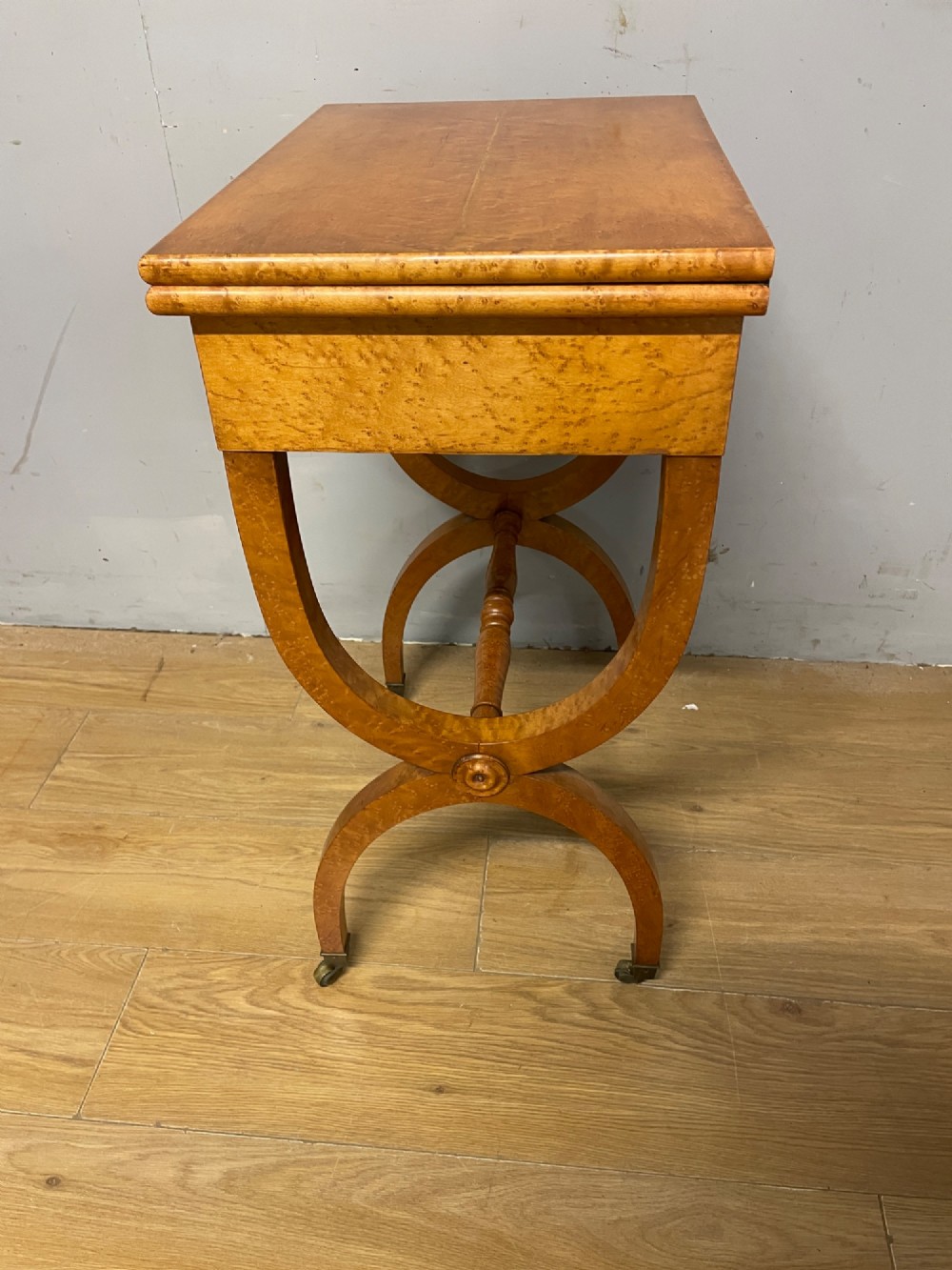 A 19th-century Biedermeier birds eye maple card table featuring a rectangular fold-over top, sweeping legs, a turned central stretcher, and brass castors. View IX