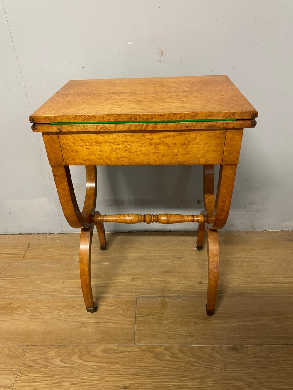 A 19th-century Biedermeier birds eye maple card table featuring a rectangular fold-over top, sweeping legs, a turned central stretcher, and brass castors. View X