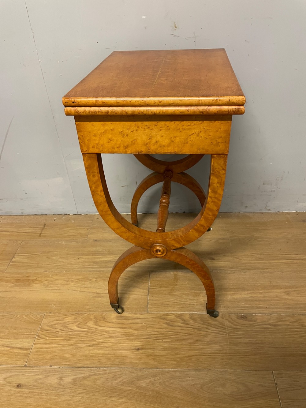 A 19th-century Biedermeier birds eye maple card table featuring a rectangular fold-over top, sweeping legs, a turned central stretcher, and brass castors. View XI