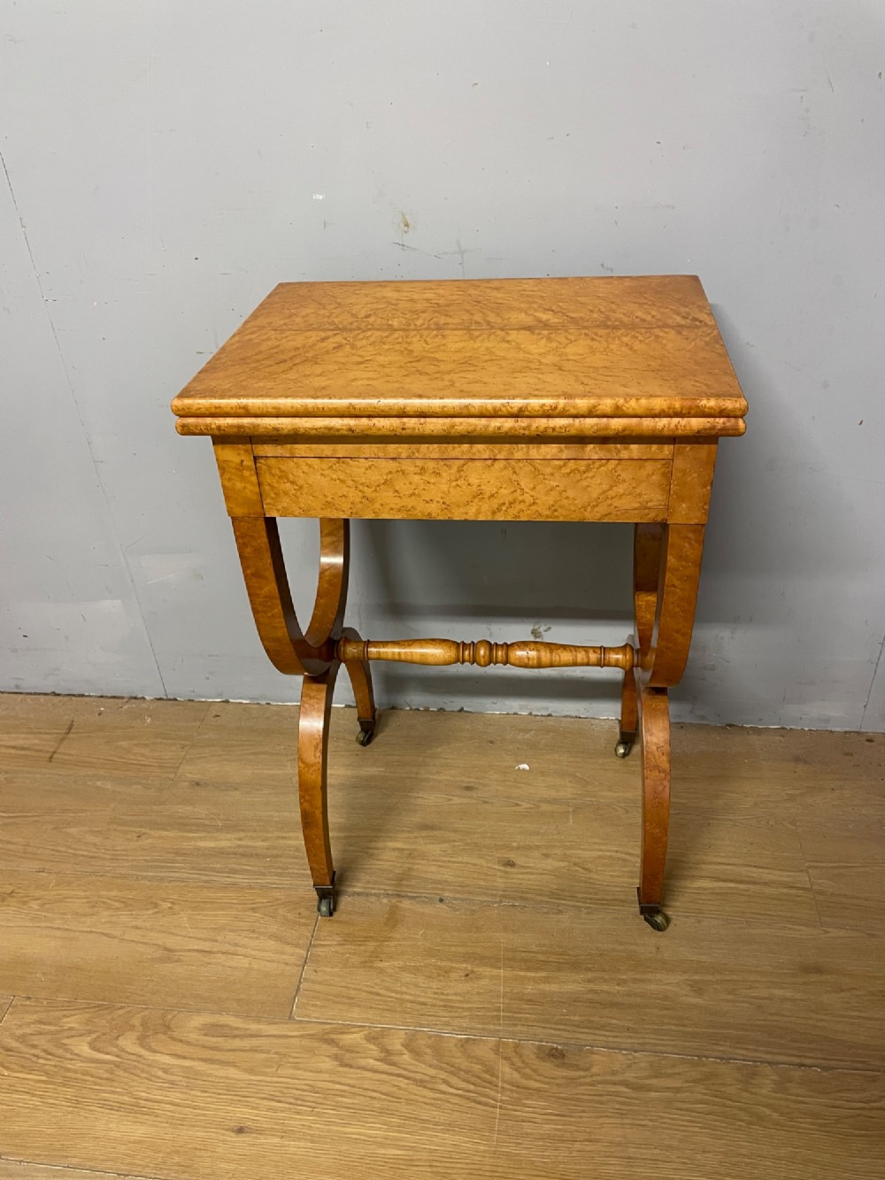 A 19th-century Biedermeier birds eye maple card table featuring a rectangular fold-over top, sweeping legs, a turned central stretcher, and brass castors. View XII