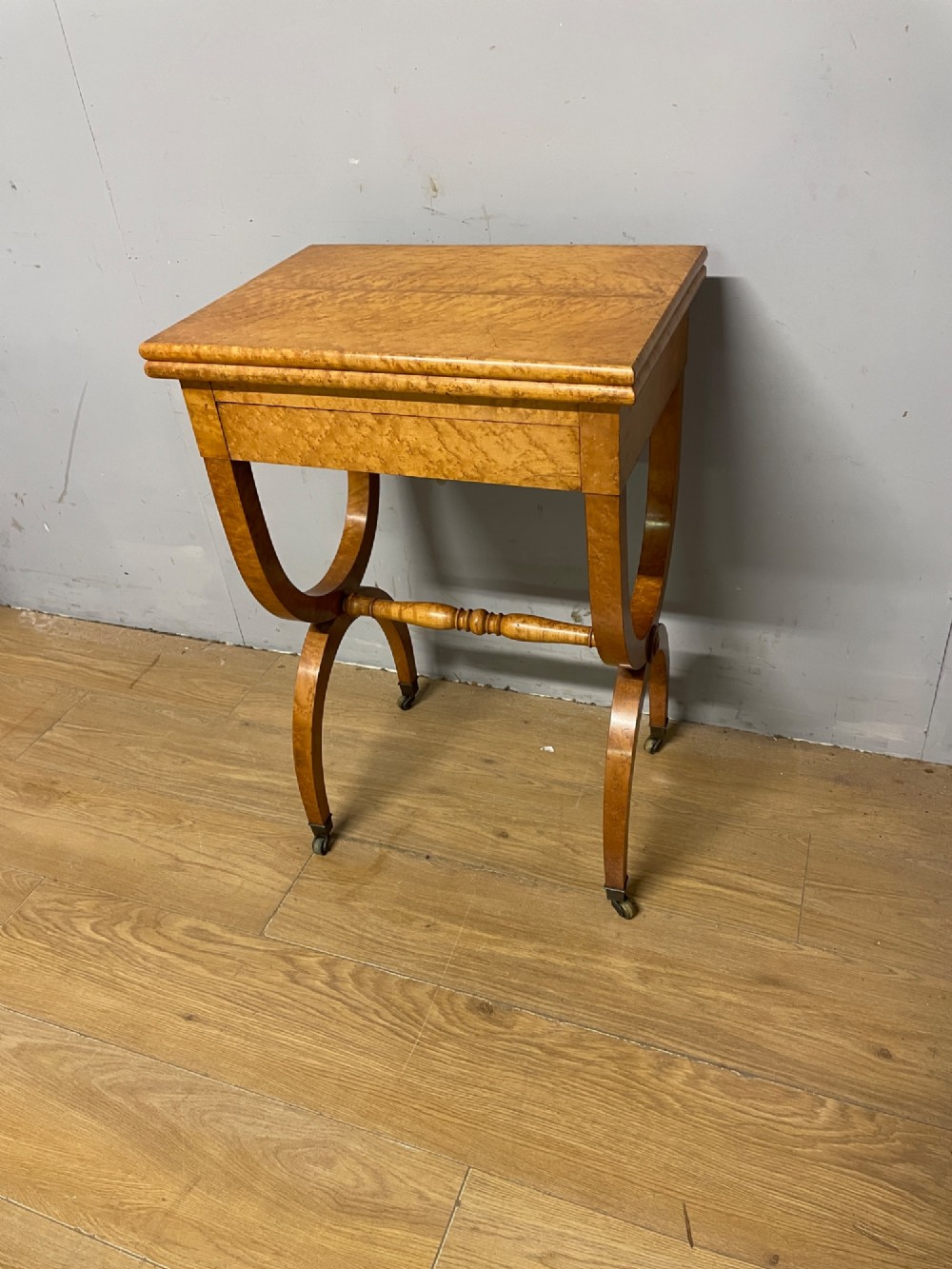 A 19th-century Biedermeier birds eye maple card table featuring a rectangular fold-over top, sweeping legs, a turned central stretcher, and brass castors. View XIII