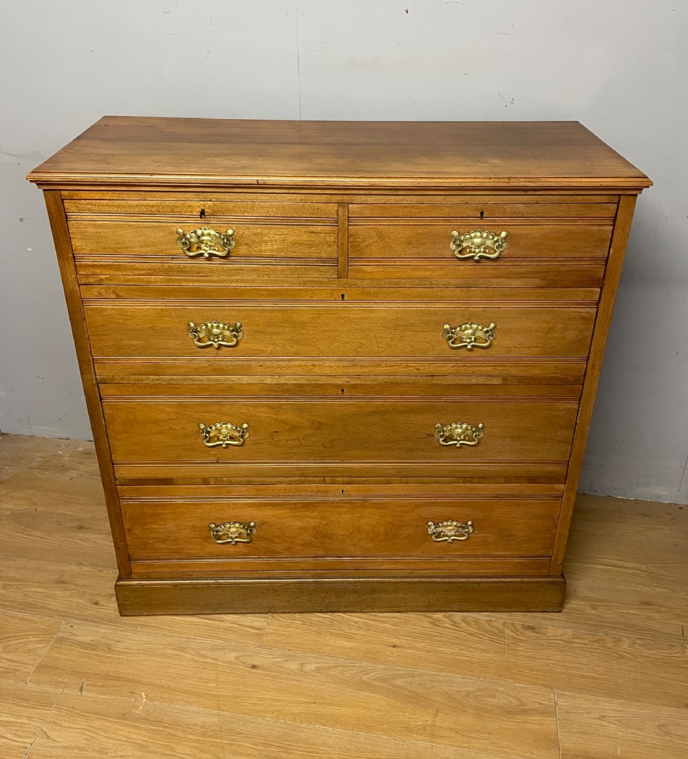 An Arts and Crafts satin walnut chest of drawers featuring two short over three long drawers with brass drop handles and a solid plinth base. View II