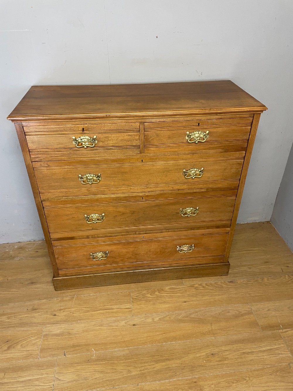 An Arts and Crafts satin walnut chest of drawers featuring two short over three long drawers with brass drop handles and a solid plinth base. View IV