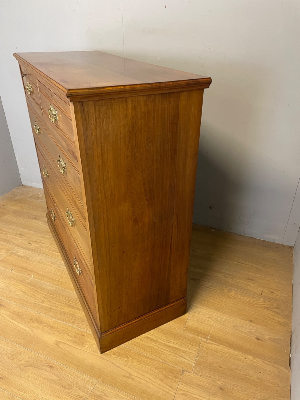 An Arts and Crafts satin walnut chest of drawers featuring two short over three long drawers with brass drop handles and a solid plinth base. View V