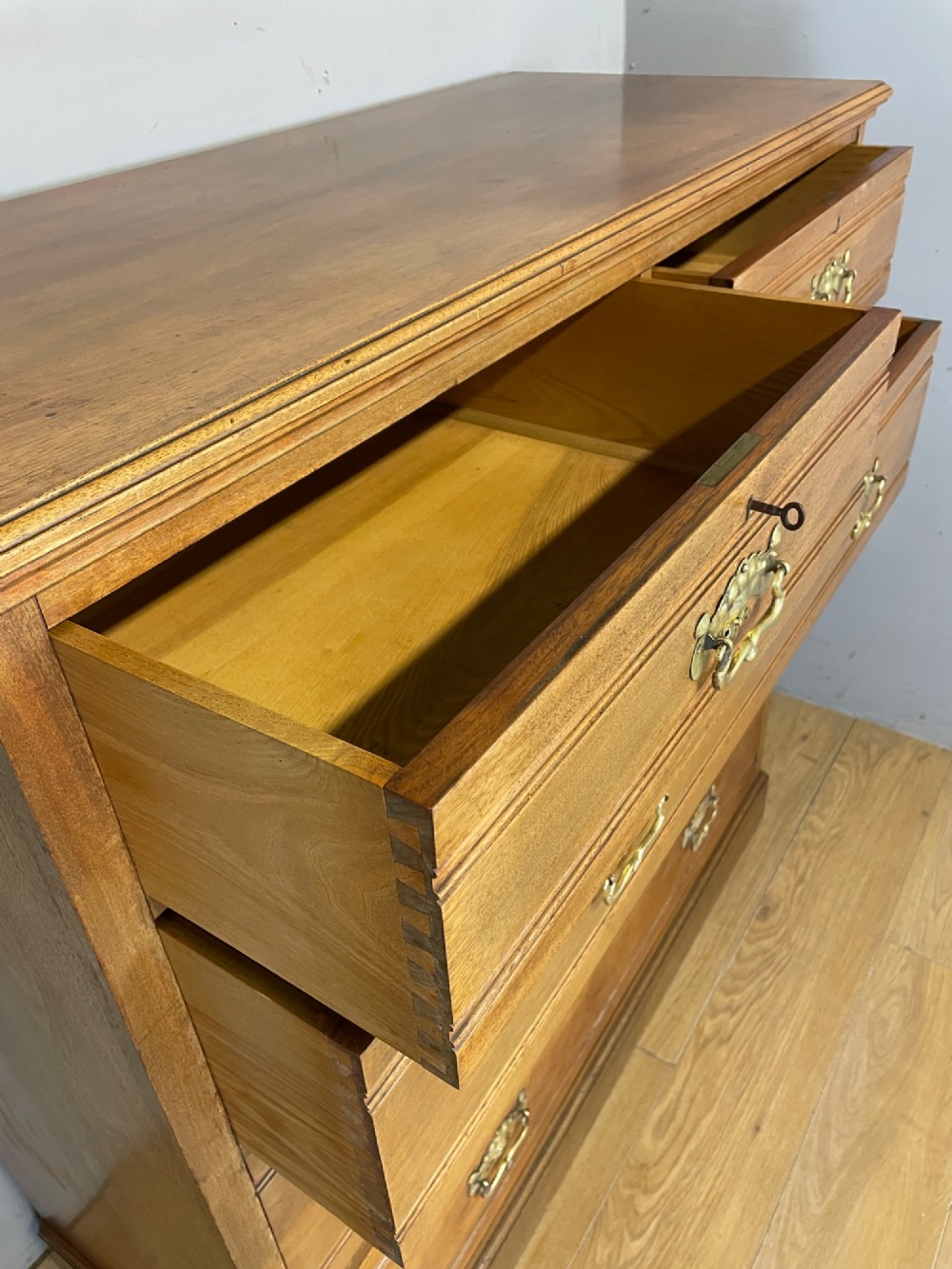 An Arts and Crafts satin walnut chest of drawers featuring two short over three long drawers with brass drop handles and a solid plinth base. View VI