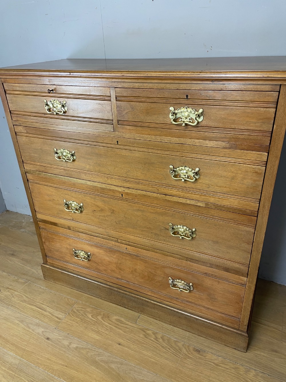 An Arts and Crafts satin walnut chest of drawers featuring two short over three long drawers with brass drop handles and a solid plinth base. View VIII