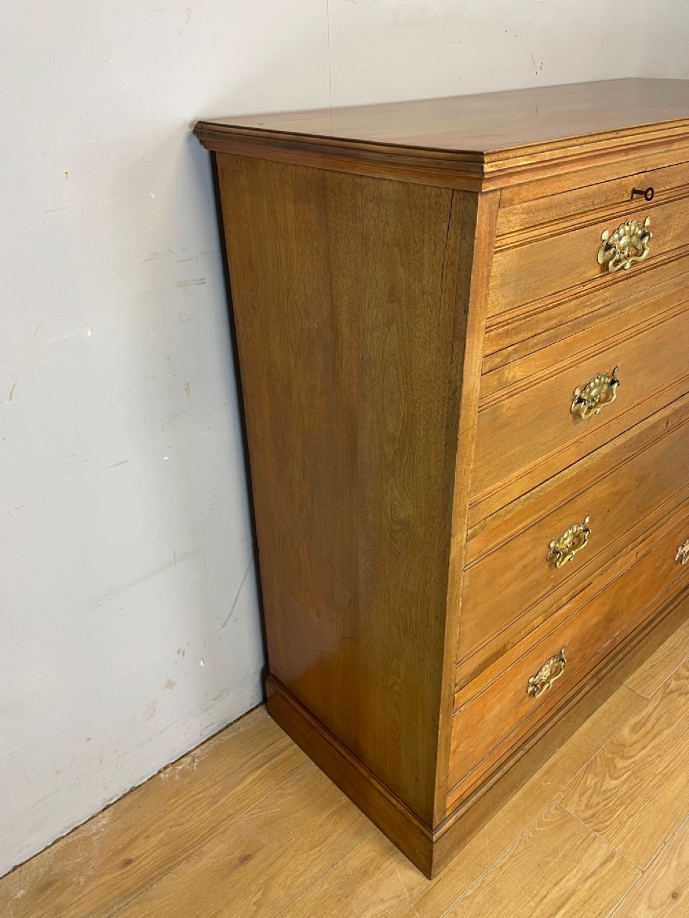 An Arts and Crafts satin walnut chest of drawers featuring two short over three long drawers with brass drop handles and a solid plinth base. View IX