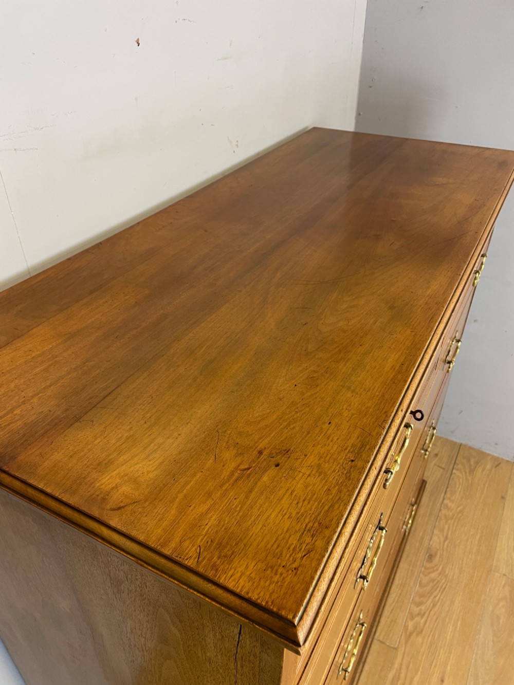 An Arts and Crafts satin walnut chest of drawers featuring two short over three long drawers with brass drop handles and a solid plinth base. View X