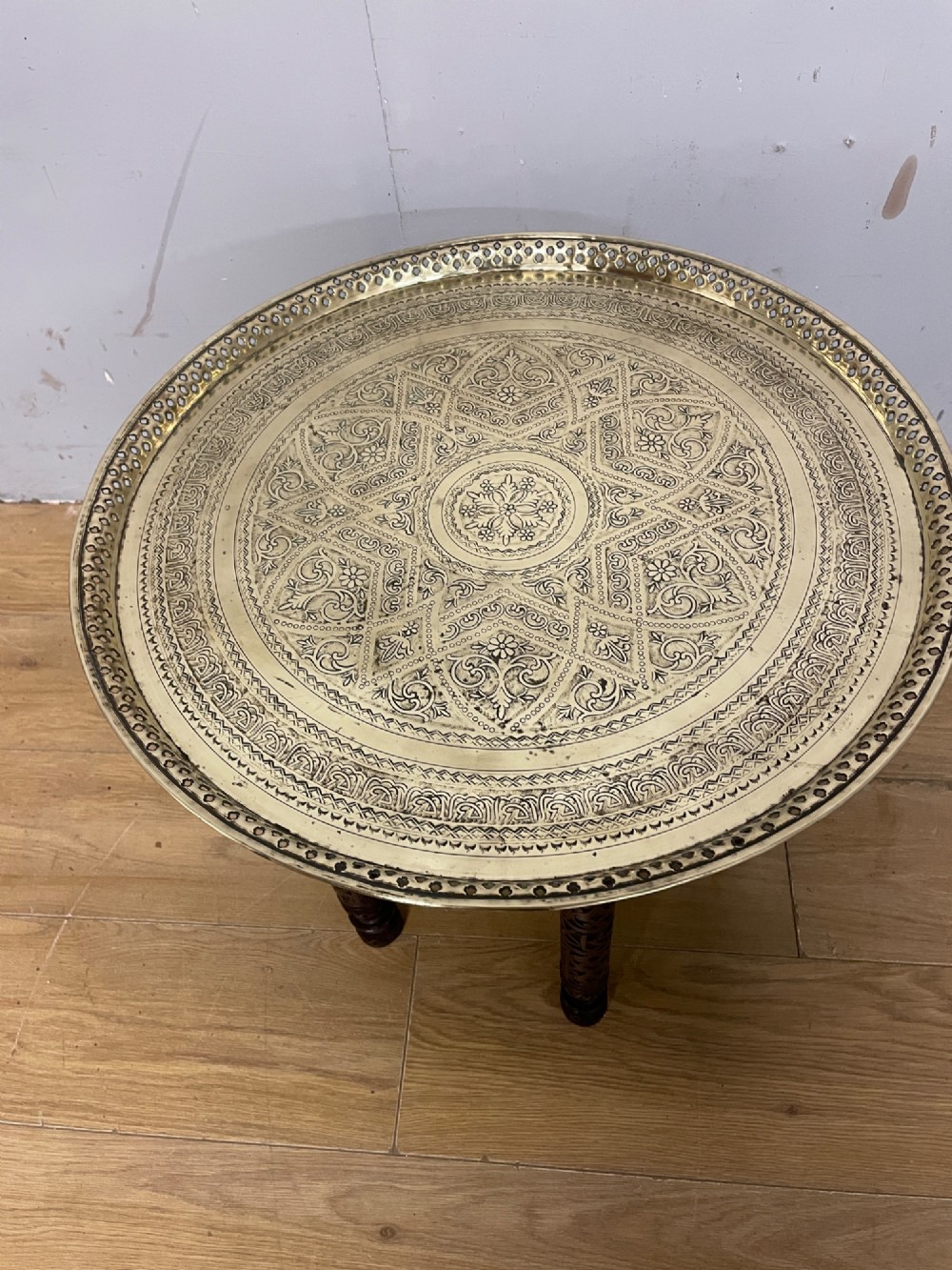 A late 19th-century Anglo-Indian Benares table featuring an intricately engraved circular brass tray top resting on a dark carved wooden folding base. View II