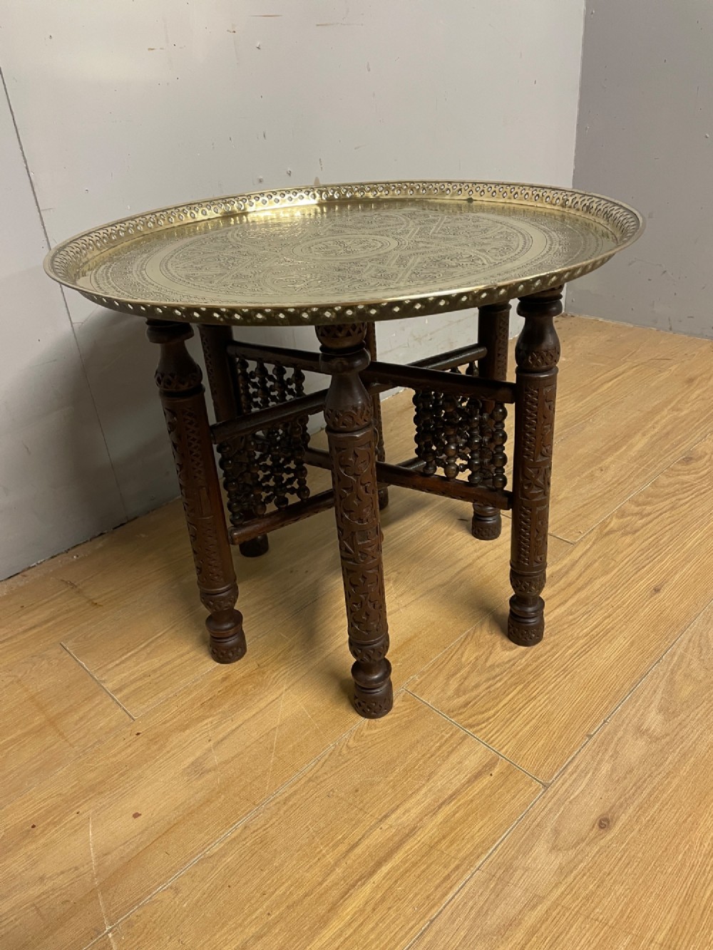 A late 19th-century Anglo-Indian Benares table featuring an intricately engraved circular brass tray top resting on a dark carved wooden folding base. View IV